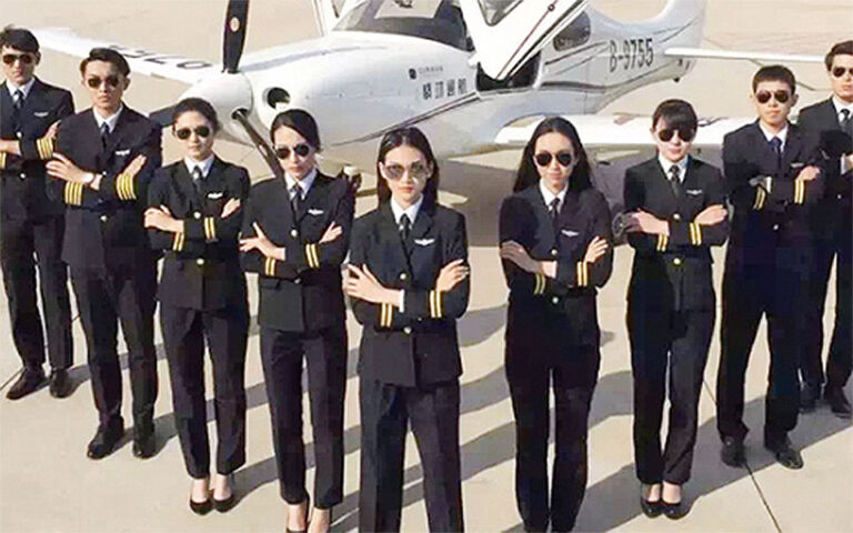 A group of eight pilots dressed in dark blue uniforms stand with arms crossed in front of a small airplane.